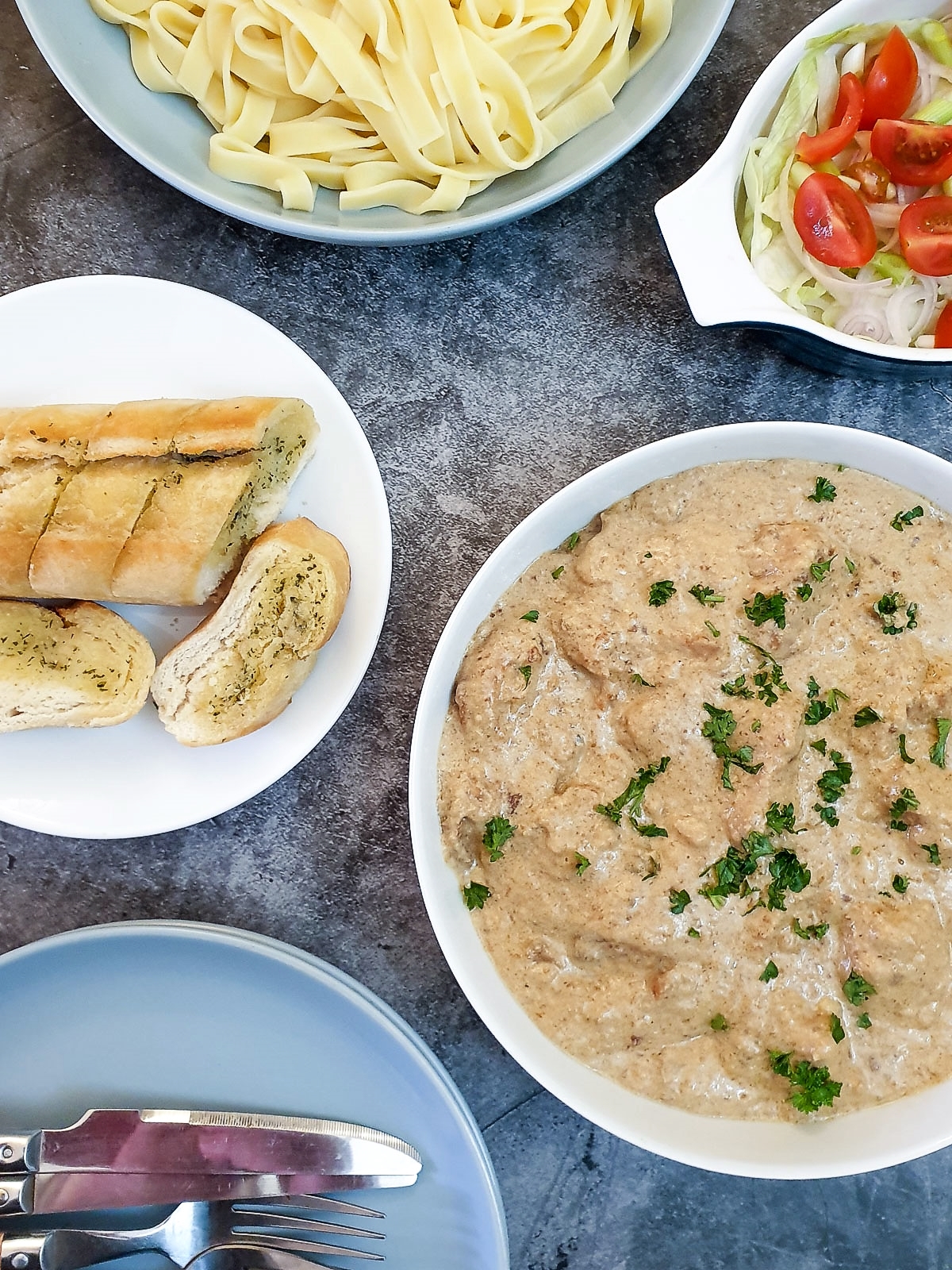 Creamy garlic mushroom chicken in a white serving dish on a table with various side dishes.