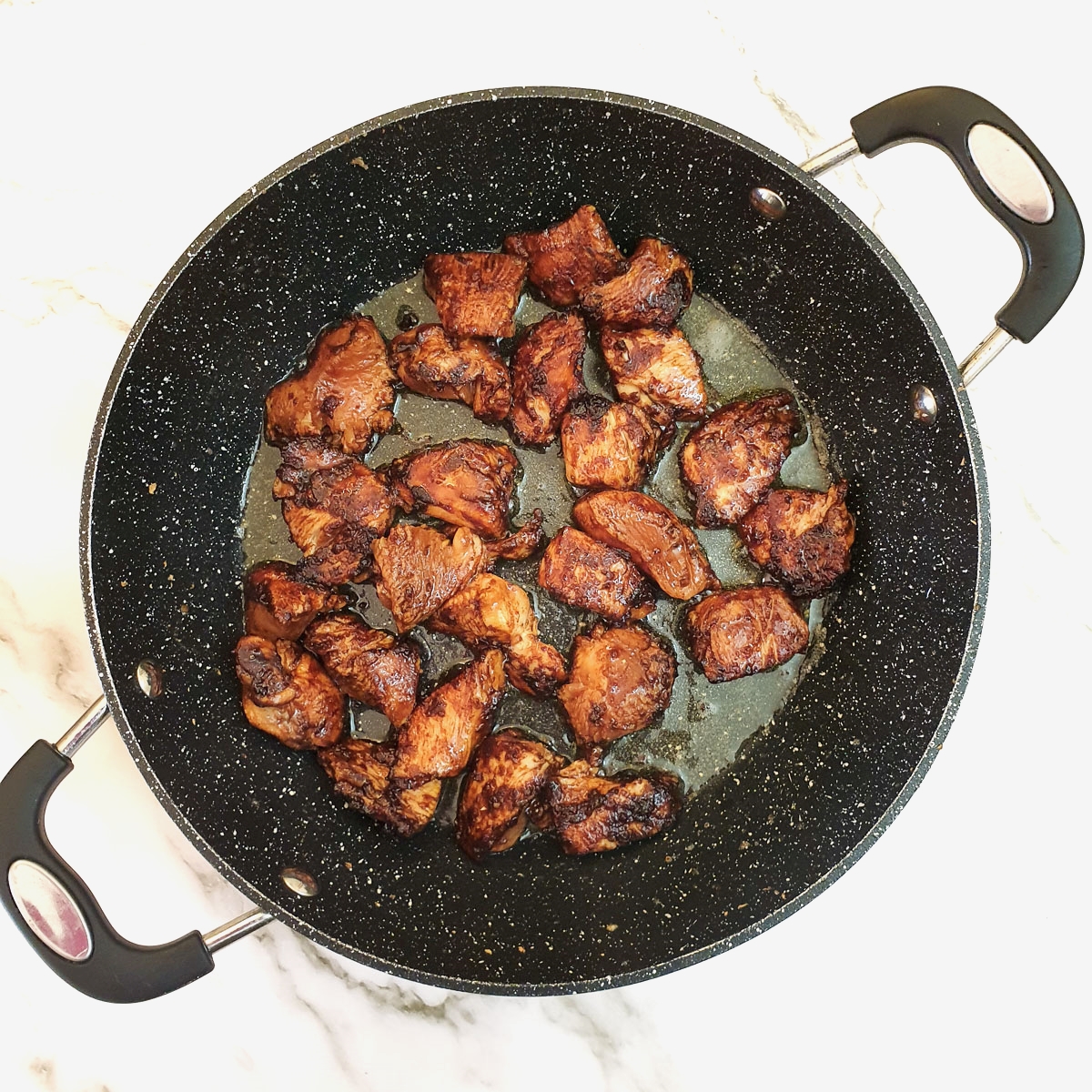 Pieces of marinated chicken browning in a frying pan.