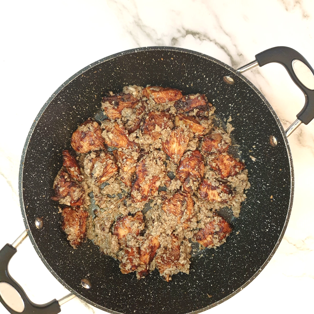 Browned chicken in pan with finely chopped mushrooms.