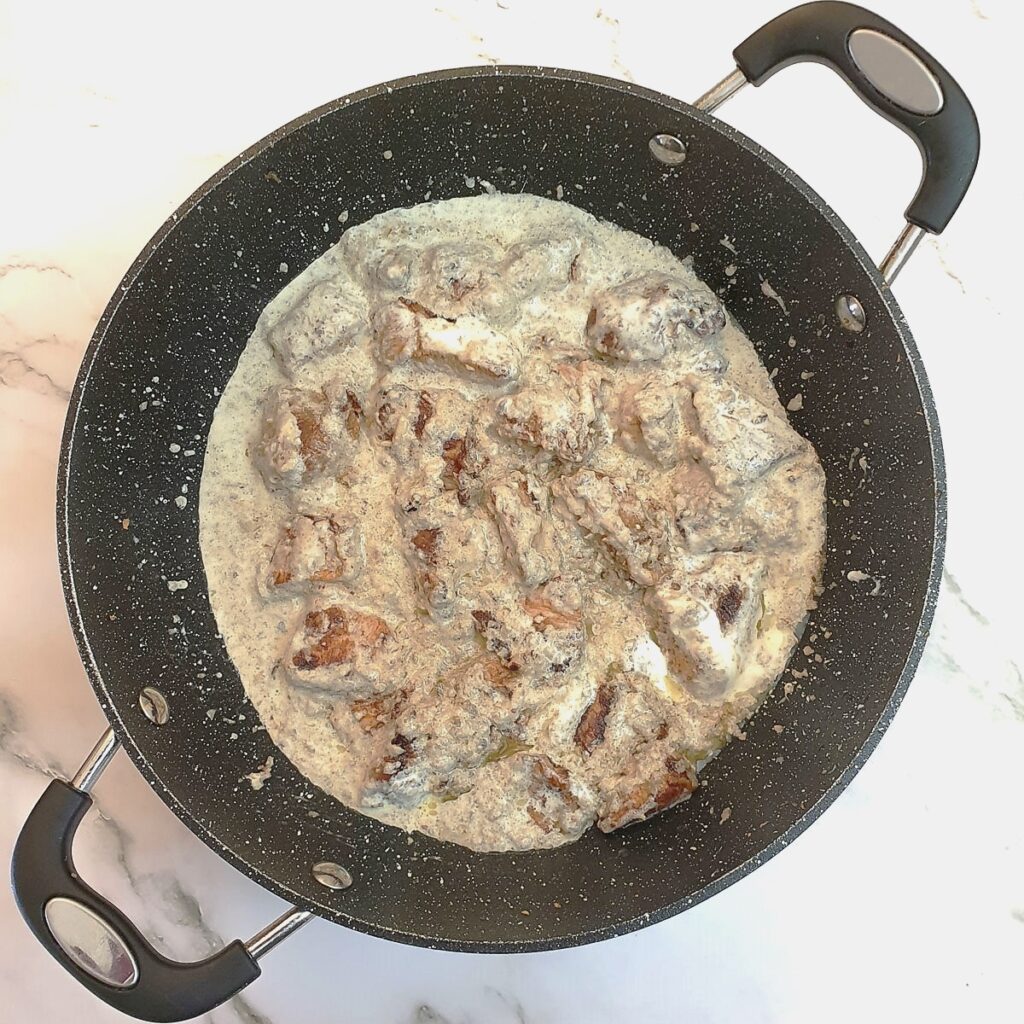 Chicken and mushrooms in a frying pan covered with cream.