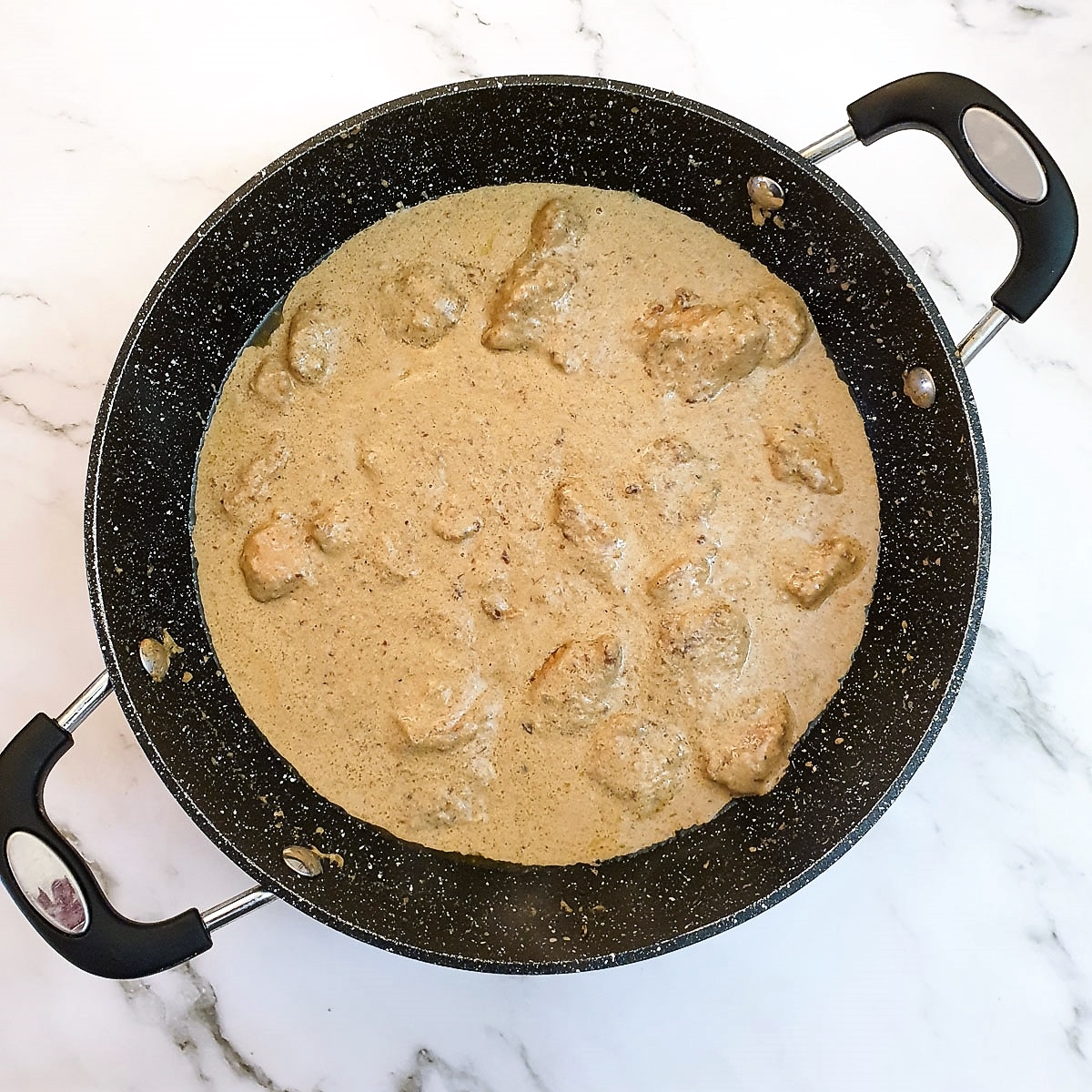 A frying pan with the result of chicken in creamy garlic mushroom sauce.