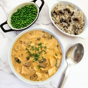 A dish of chicken Diane next to a bowl of peas and a dish of rice.