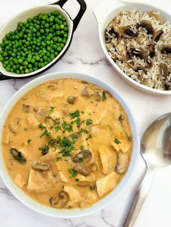 A dish of chicken Diane next to a bowl of peas and a dish of rice.