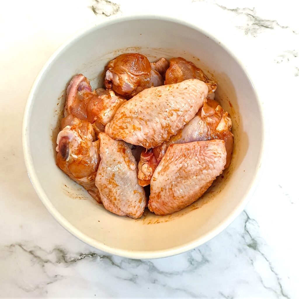 A mixing bowl containing chicken wings which have been rubbed with salt and paprika.