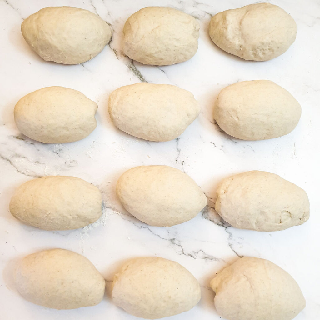 12 dough balls arranged seam-side down waiting to rise.