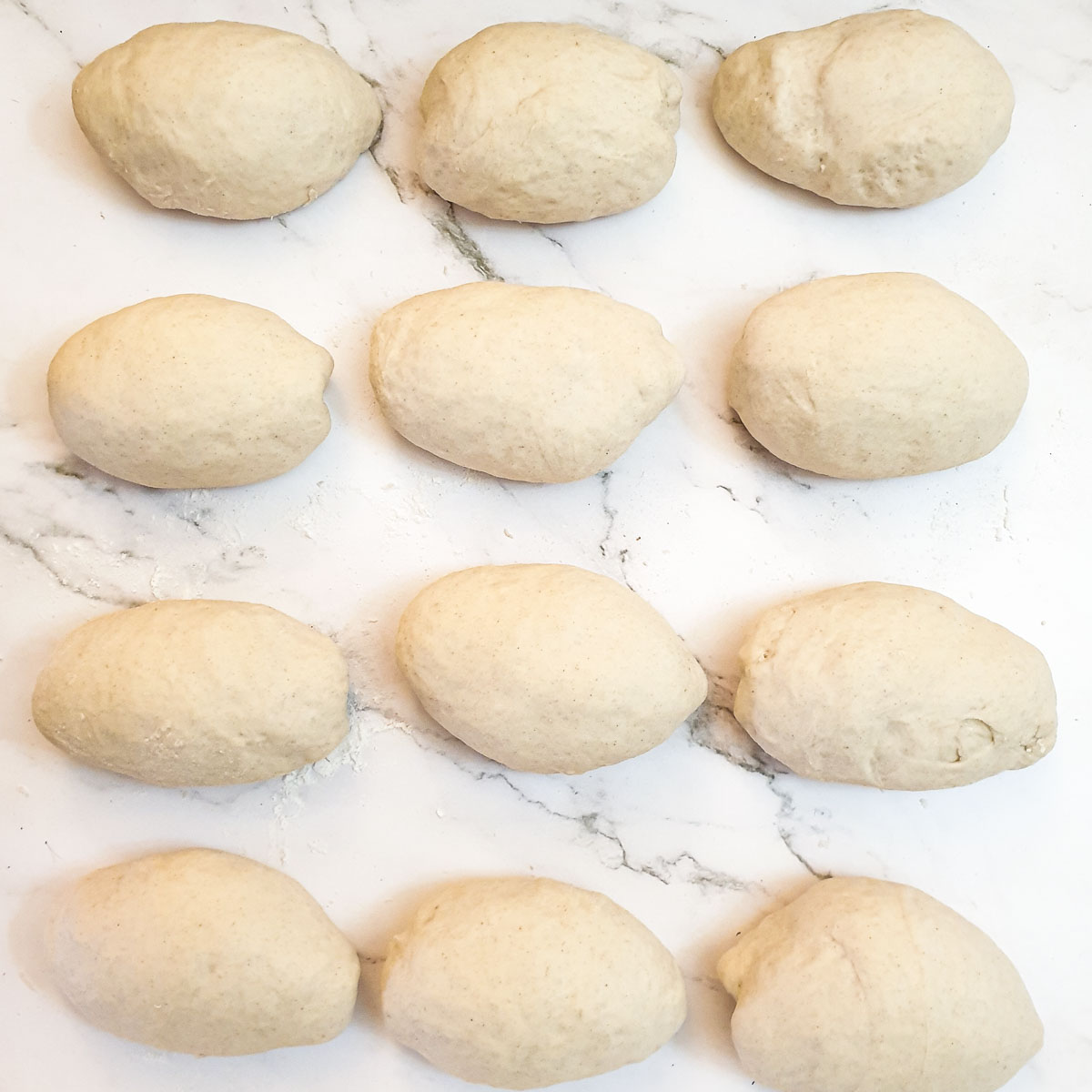 12 dough balls arranged seam-side down waiting to rise.