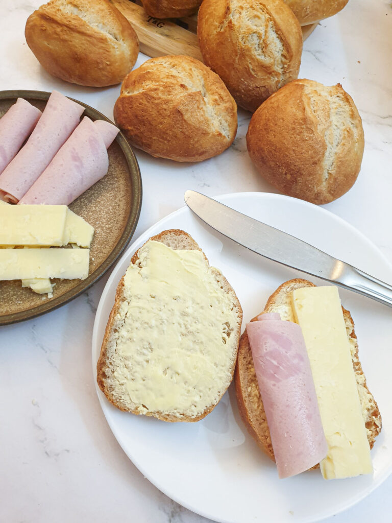 A German bread roll cut in half and spread with butter, topped with ham and cheese.