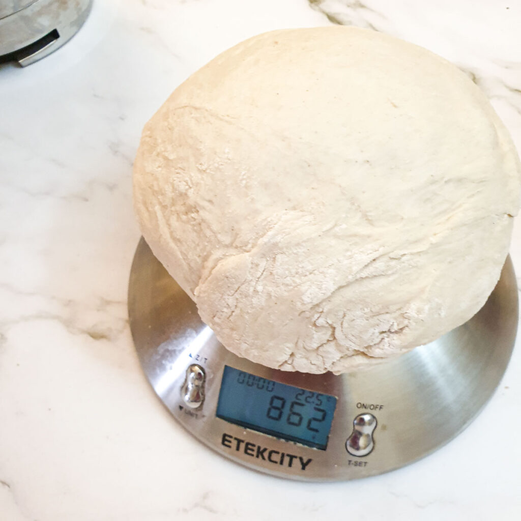The ball of dough being weighed on a scale.