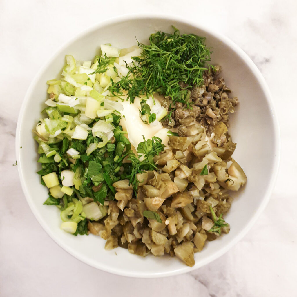 Chopped gherkins, capers, parsley and dill in a bowl with mayonnaise.