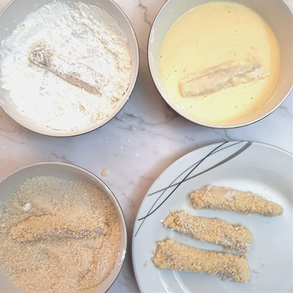 Pieces of fish being coated with cornflour, egg and breadcrumbs.