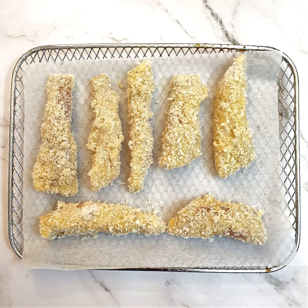 Coated fish fingers on an air-fryer baking tray.