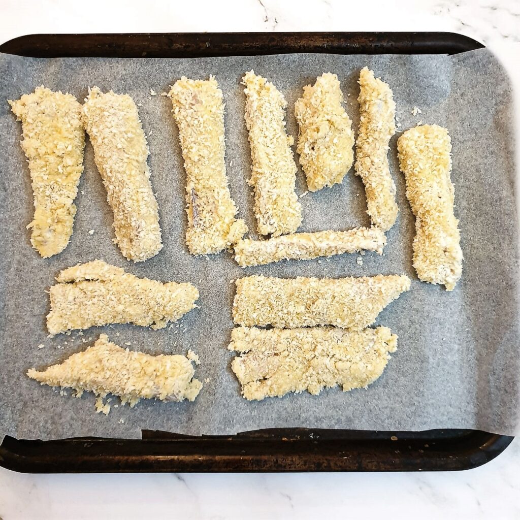 A single layer of fish fingers on a a baking tray.