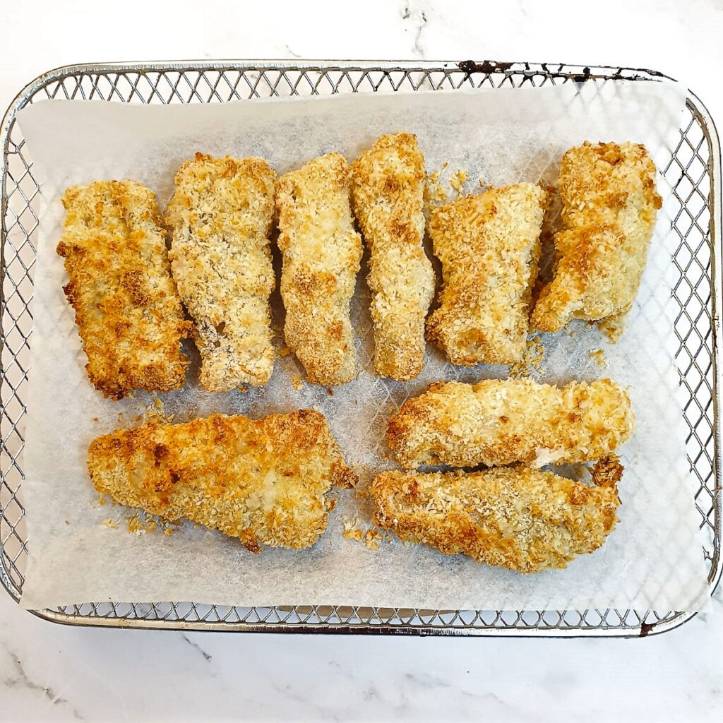 Golden brown fish fingers on a baking tray after being cooked.