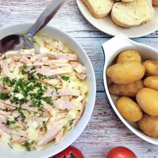 A dish of German meat salad next to a bowl of potatoes and some crusty bread.