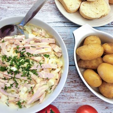 A dish of German meat salad next to a bowl of potatoes and some crusty bread.