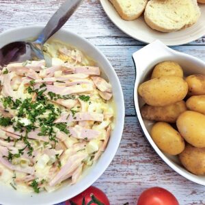 A dish of German meat salad next to a bowl of potatoes and some crusty bread.