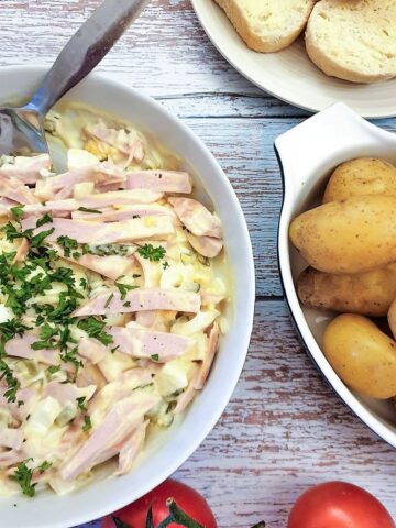 A dish of German meat salad next to a bowl of potatoes and some crusty bread.