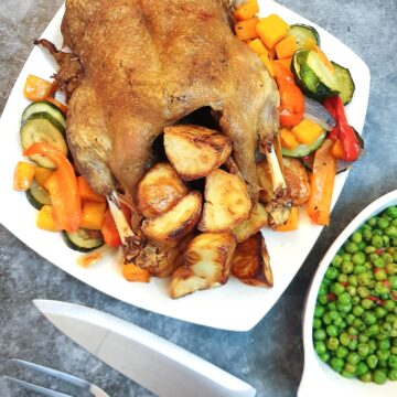 A roast duck on a serving plate with roast potatoes and vegetables.