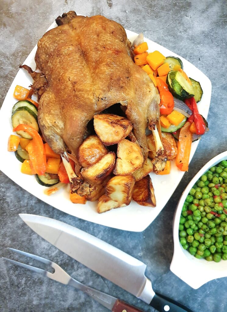 A roast duck on a serving plate with roast potatoes and vegetables.