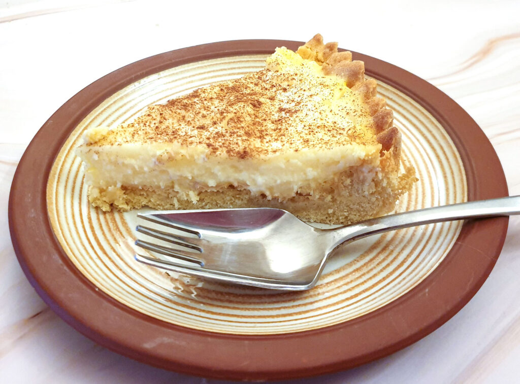 A slice of milk tart on a brown-rimmed plate with a cake fork.