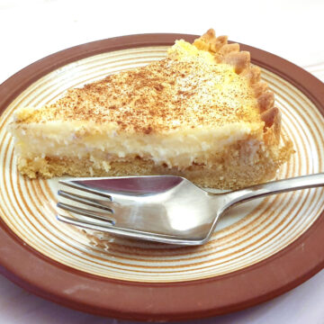 A slice of milk tart on a brown-rimmed plate with a cake fork.