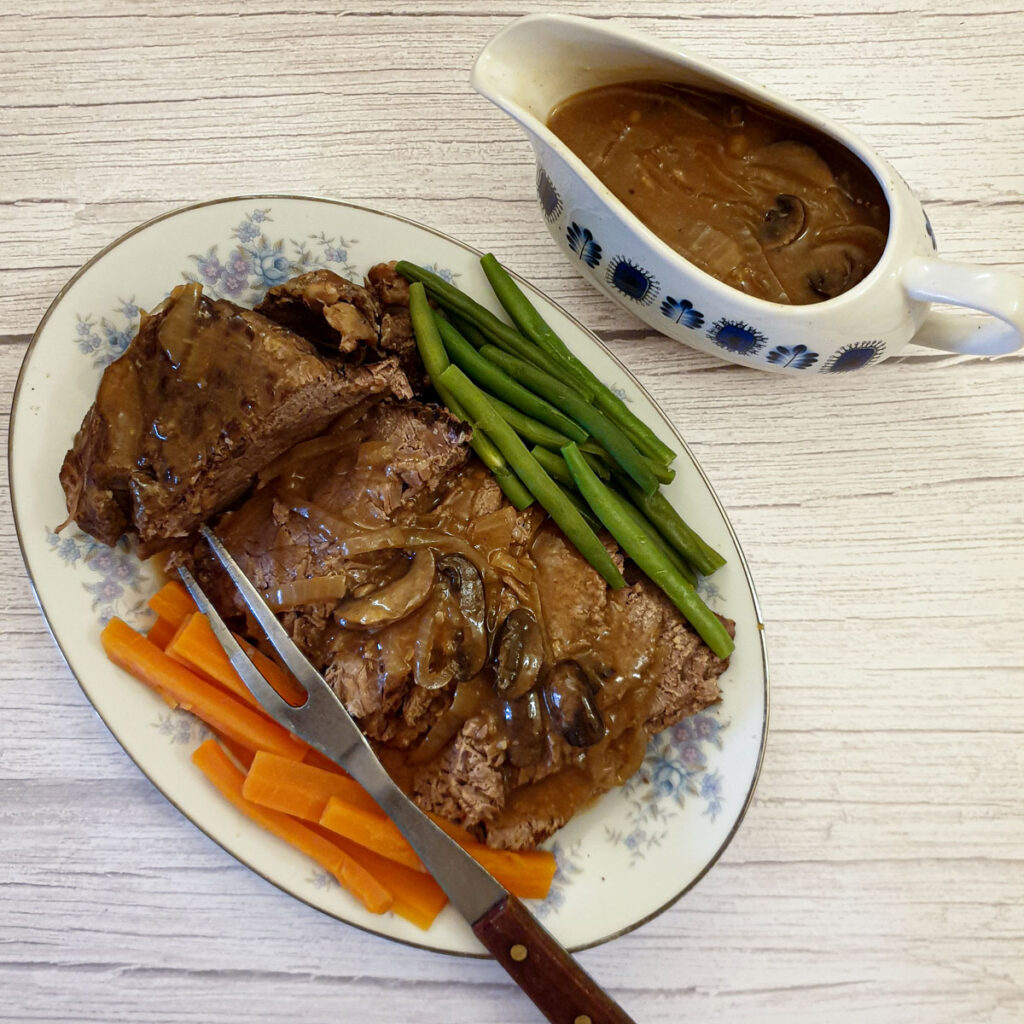 A serving plate of sliced beef topside next to a jug of gravy.