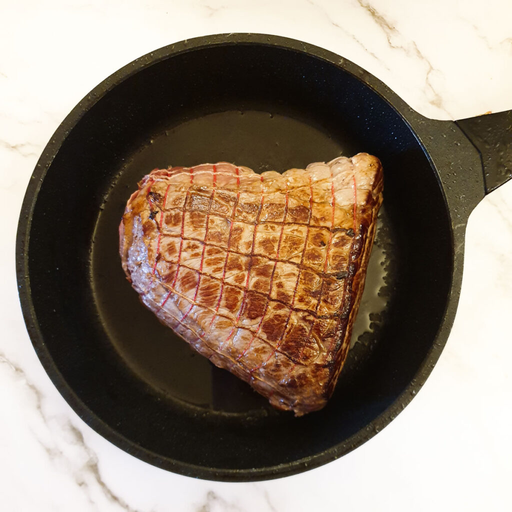 A joint of beef topside browning in a frying pan.