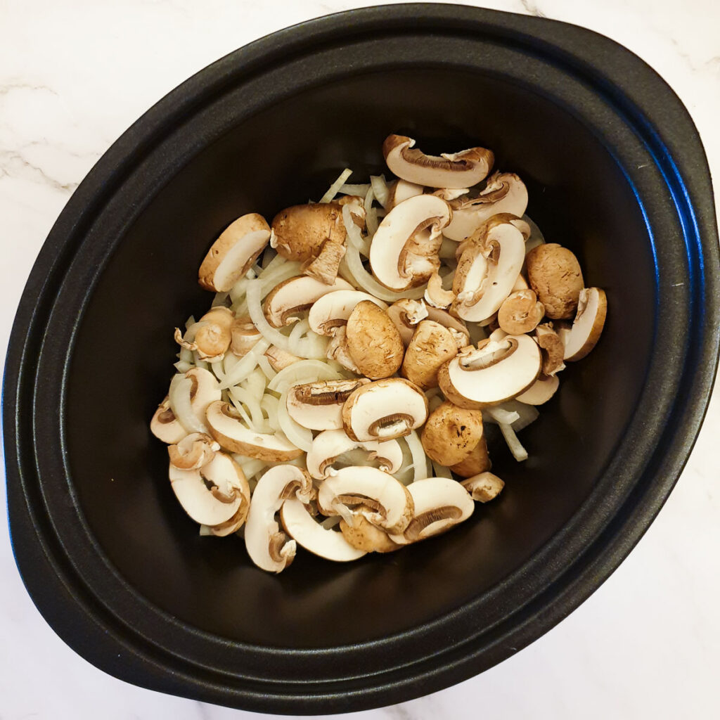 Sliced mushrooms and onions in a slow-cooker.