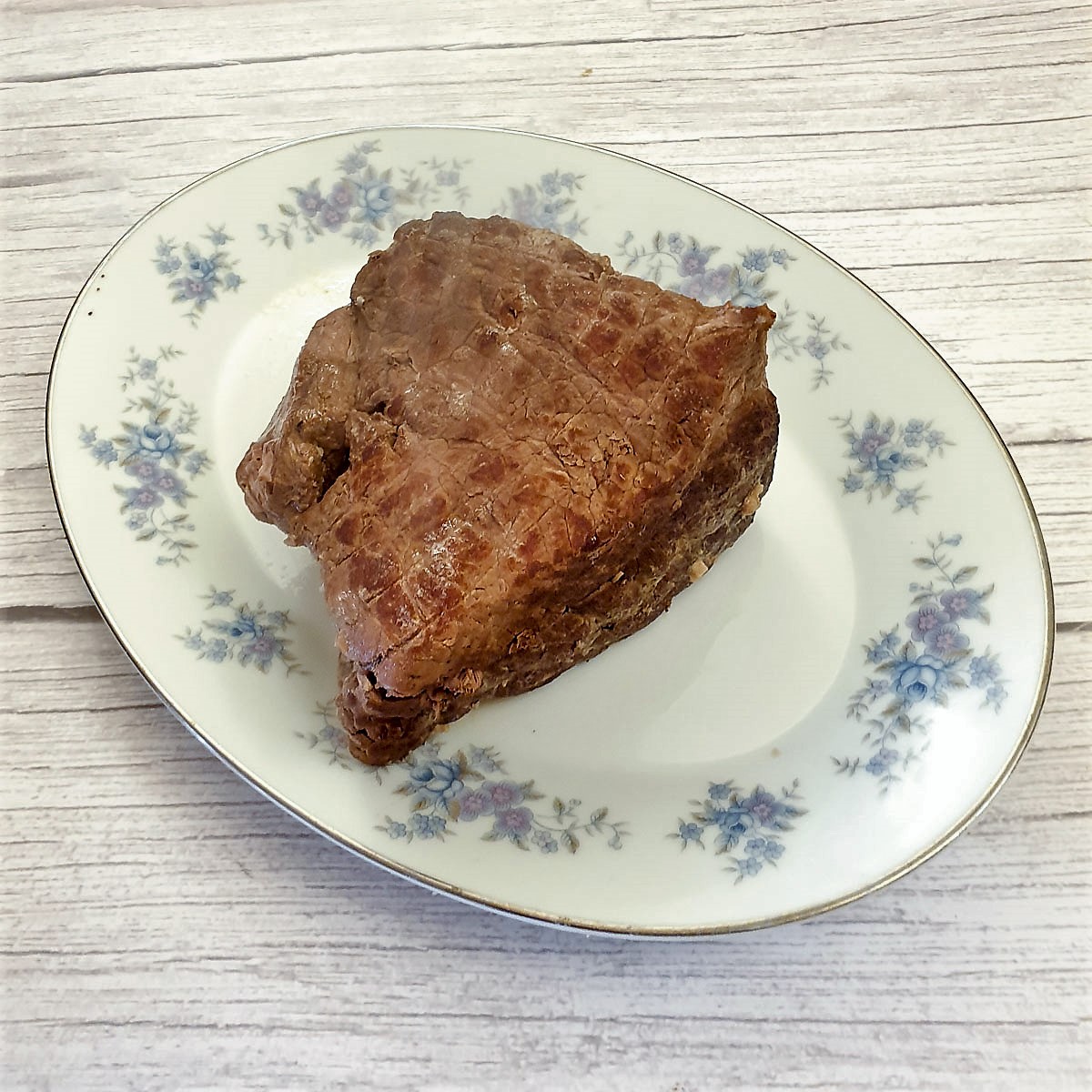 A joint of cooked beef topside on a plate.