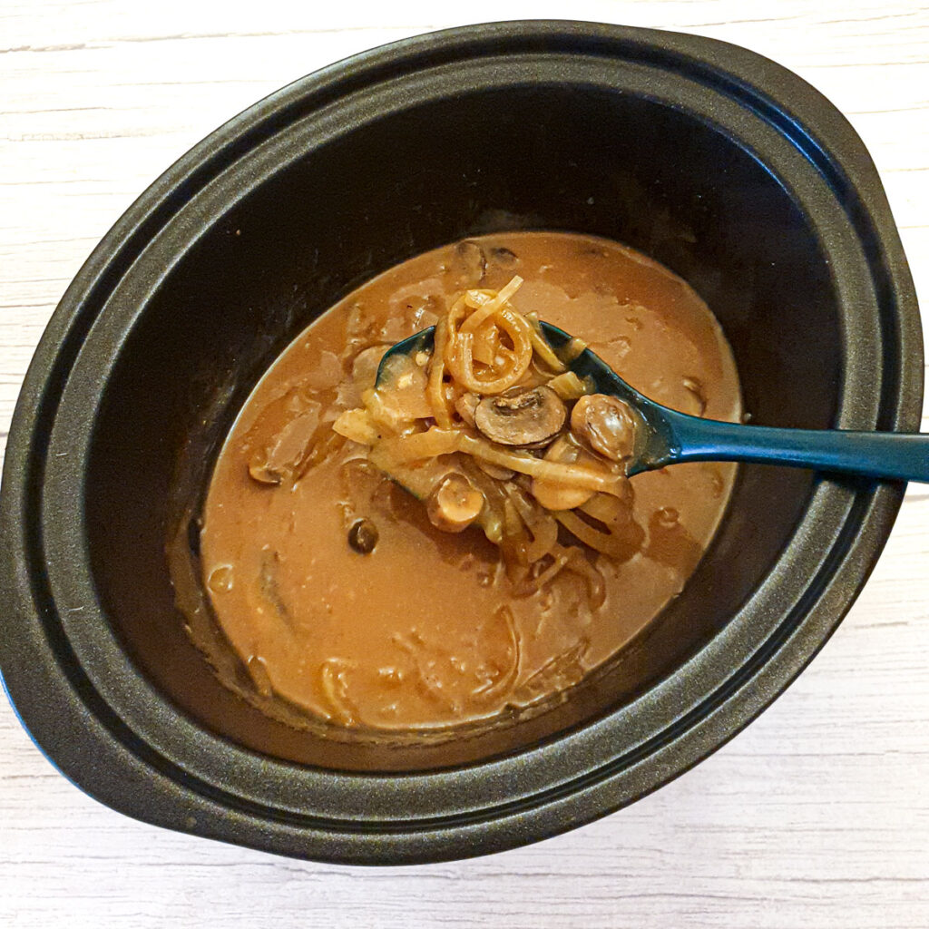 A spoonful of mushroom and onion gravy being lifted from the slow-cooker.