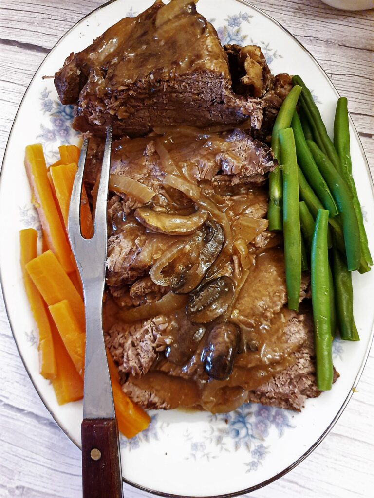 Sliced beef topside on a plate, covered with mushroom and onion gravy and surrounded with carrots and green beans.