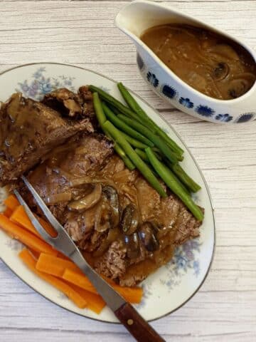 A serving plate of sliced beef topside next to a jug of gravy.