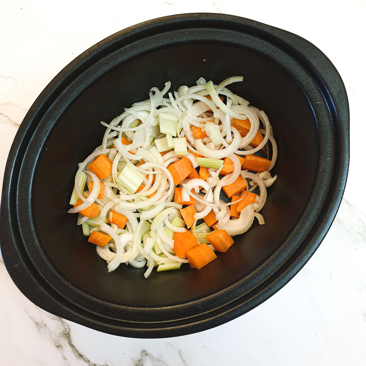 Sliced onions, carrots and celery in a slow-cooker.
