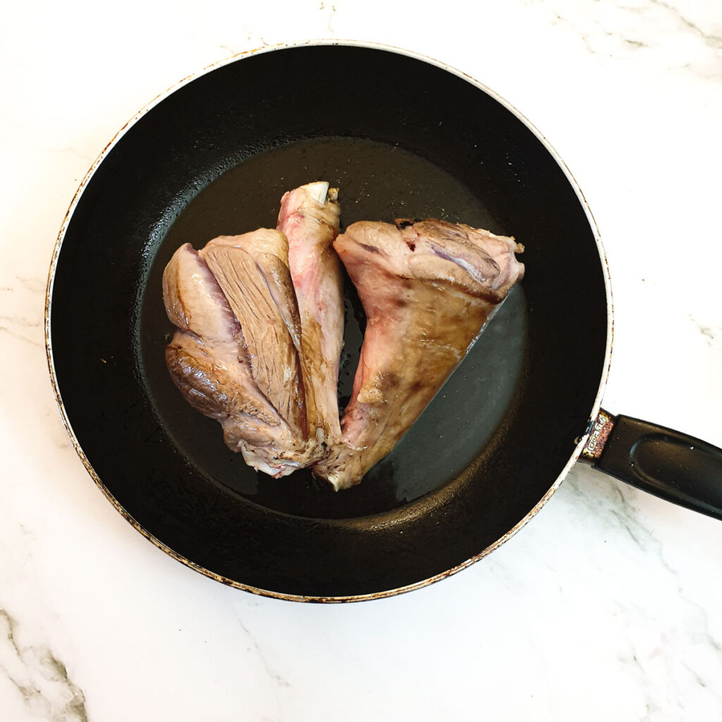 2 lamb shanks browning in a frying pan.