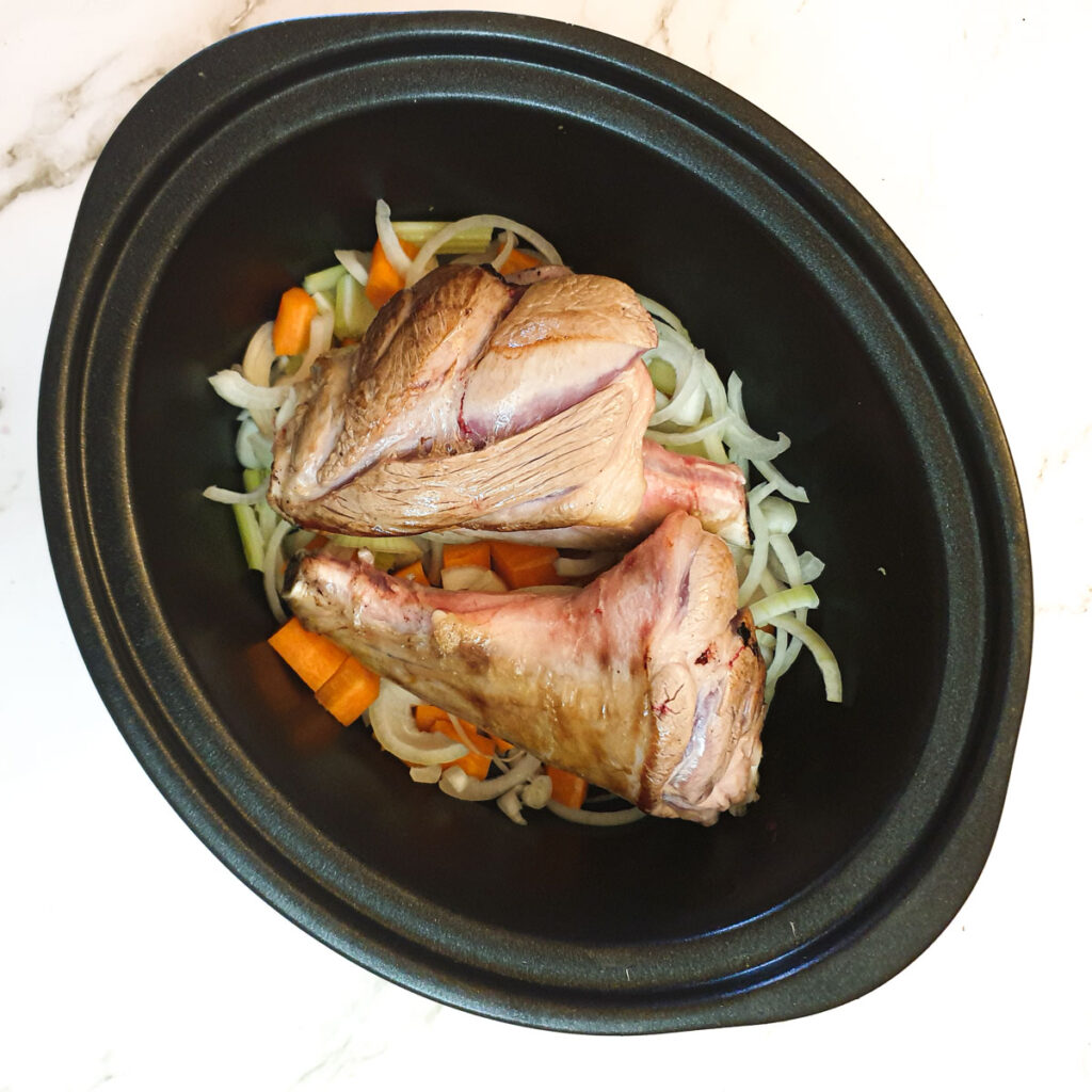 Lamb shanks on top of the vegetables in a slow-cooker.