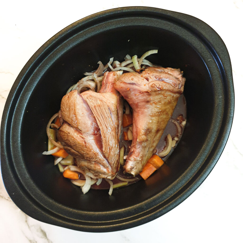 Lmb shanks and vegetables in a slow-cooker covered with stock.