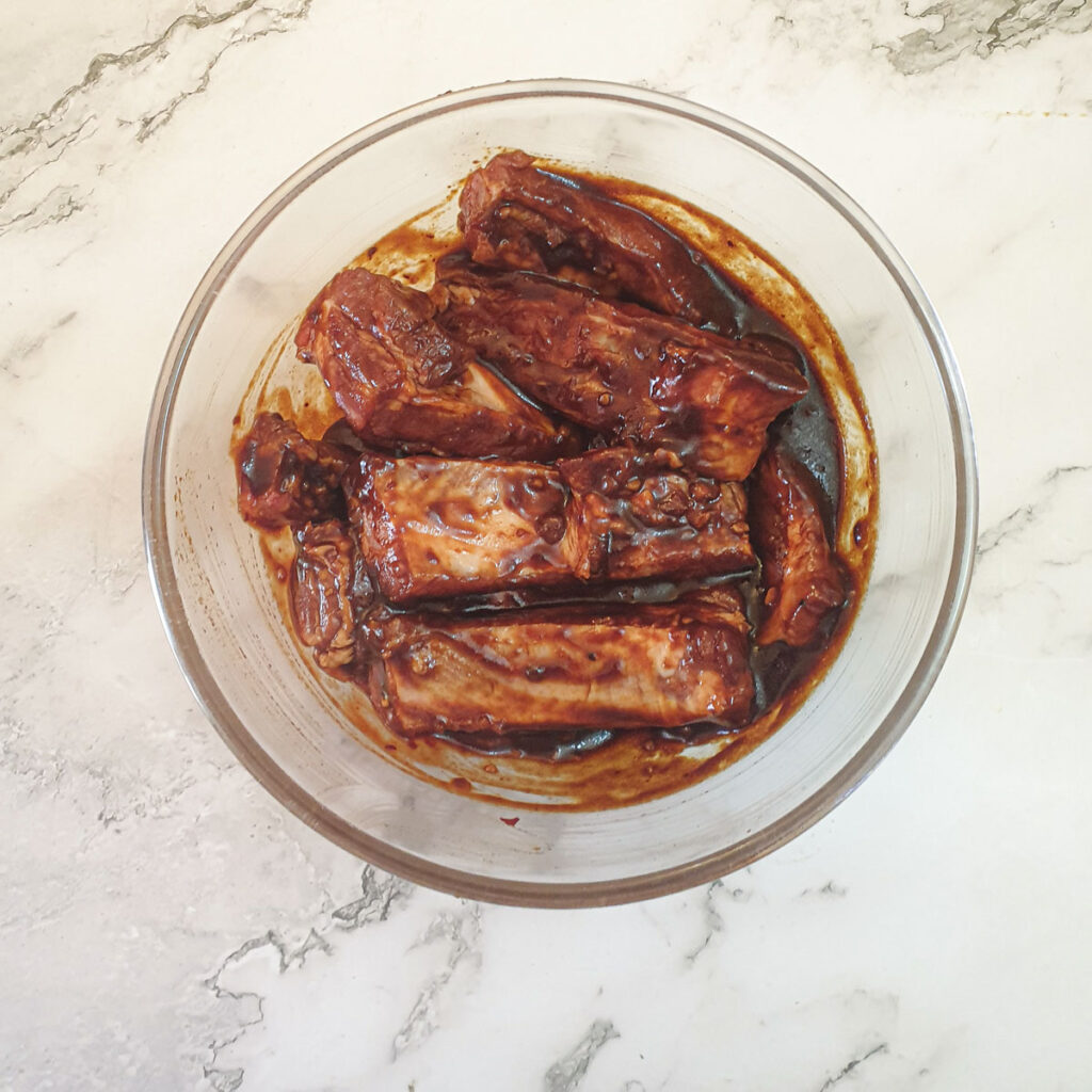 Pork ribs in a marinade in a glass bowl.