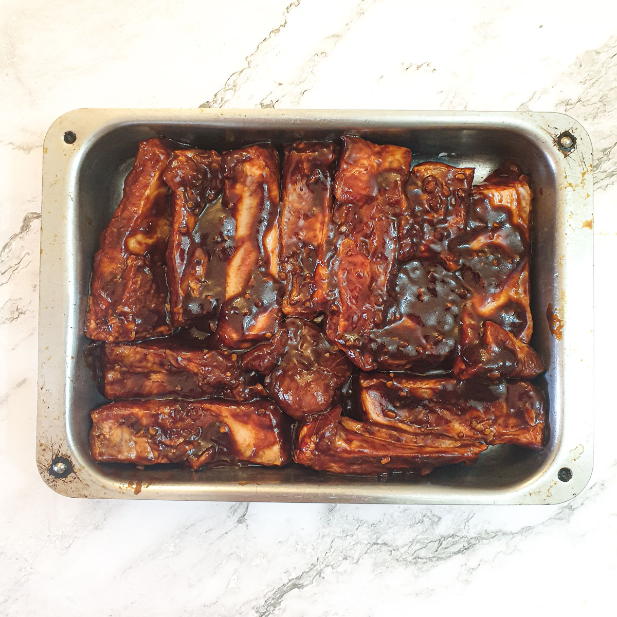 Unbaked ribs arranged in a single layer in a metal baking dish.
