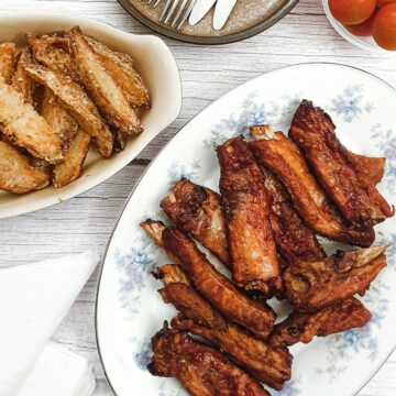 Sticky pork ribs on plate next to a dish of potato wedges.