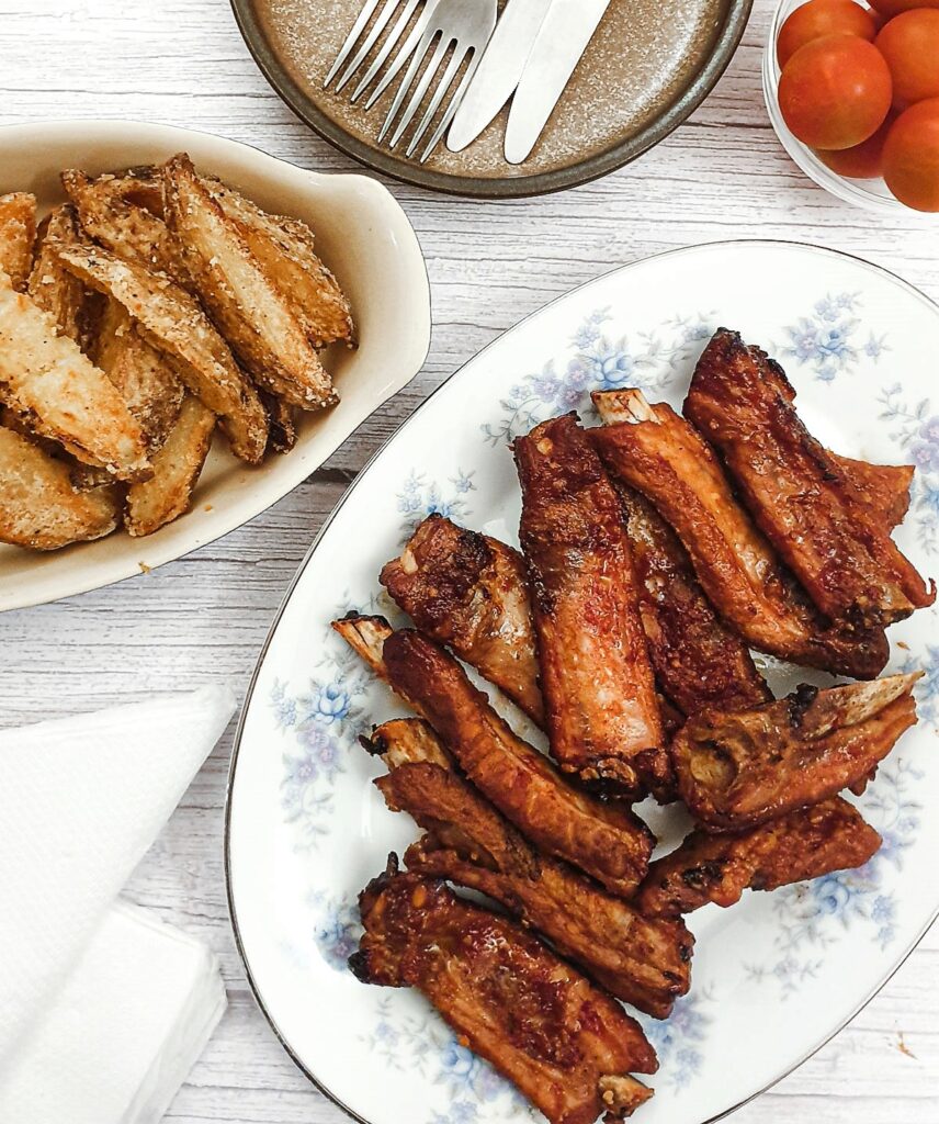 Sticky pork ribs on  plate next to a dish of potato wedges.