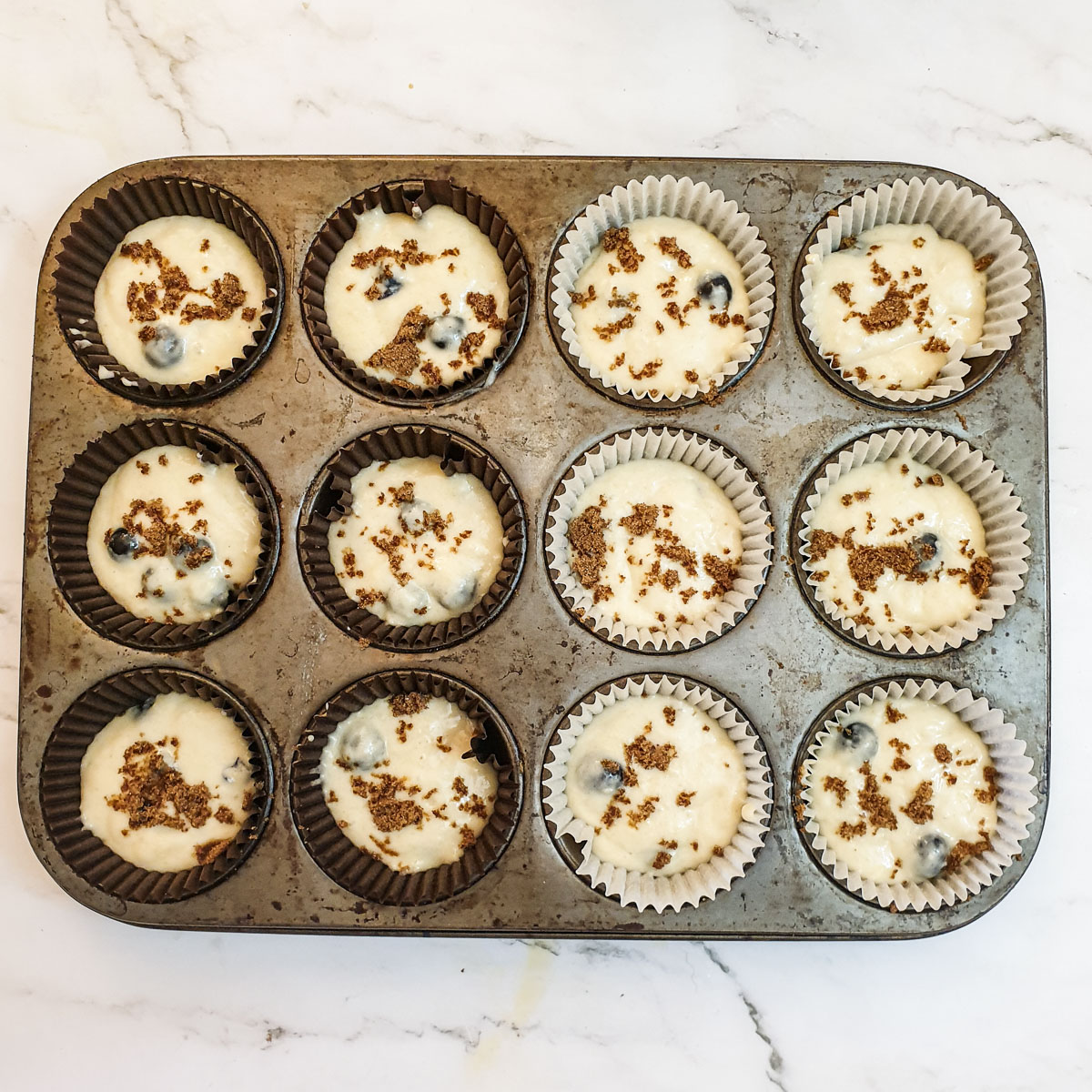 12 blueberry muffins in a muffin tray ready to go into the oven.