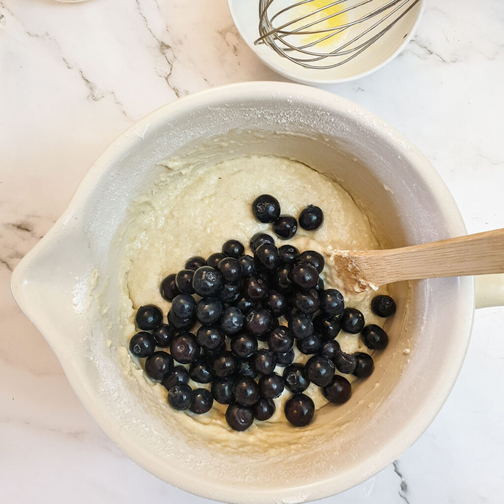 Blueberries and muffin batter in a mixing bowl.