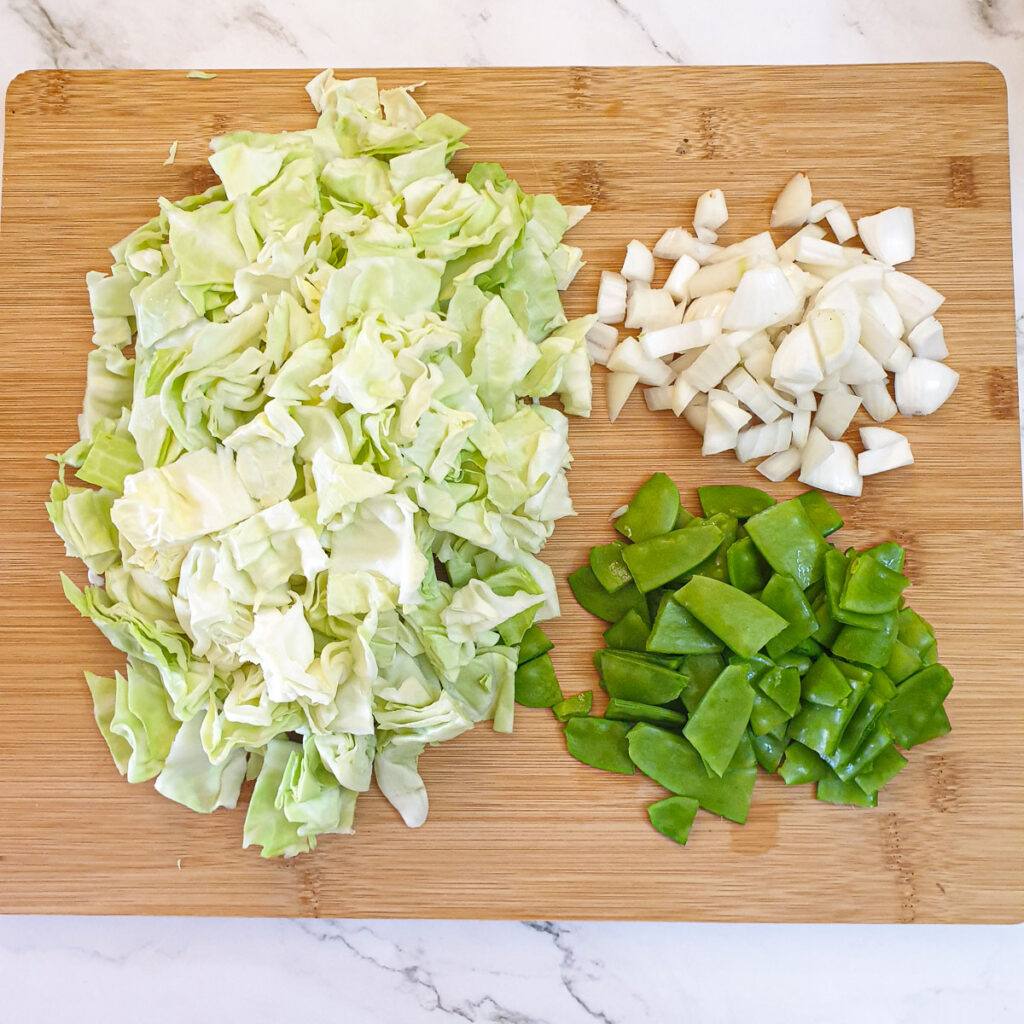 Chopped cabbage, sugar snaps and onions on a chopping board.