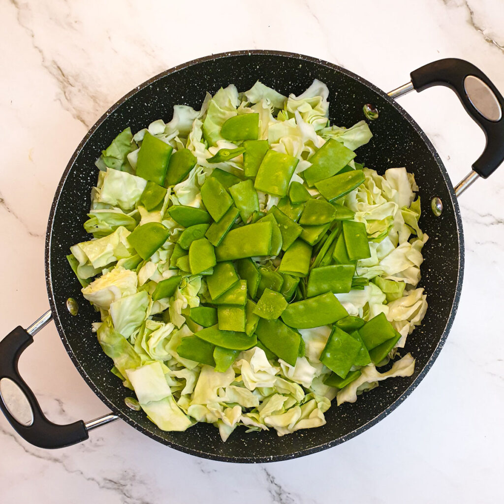 Cabbage and sugar snaps in a frying pan.