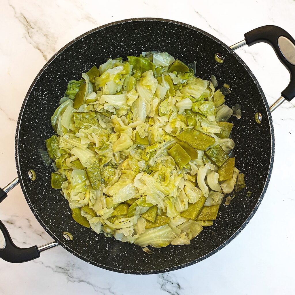 Cooked cabbage and sugar snaps in a frying pan.