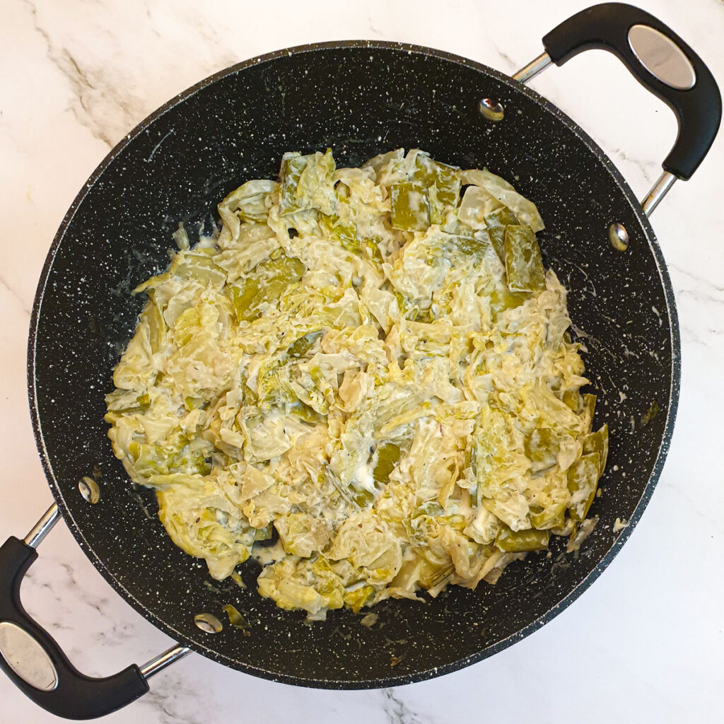 A frying pan containing the braised cabbage and sugar snap peas mixed with cream cheese.