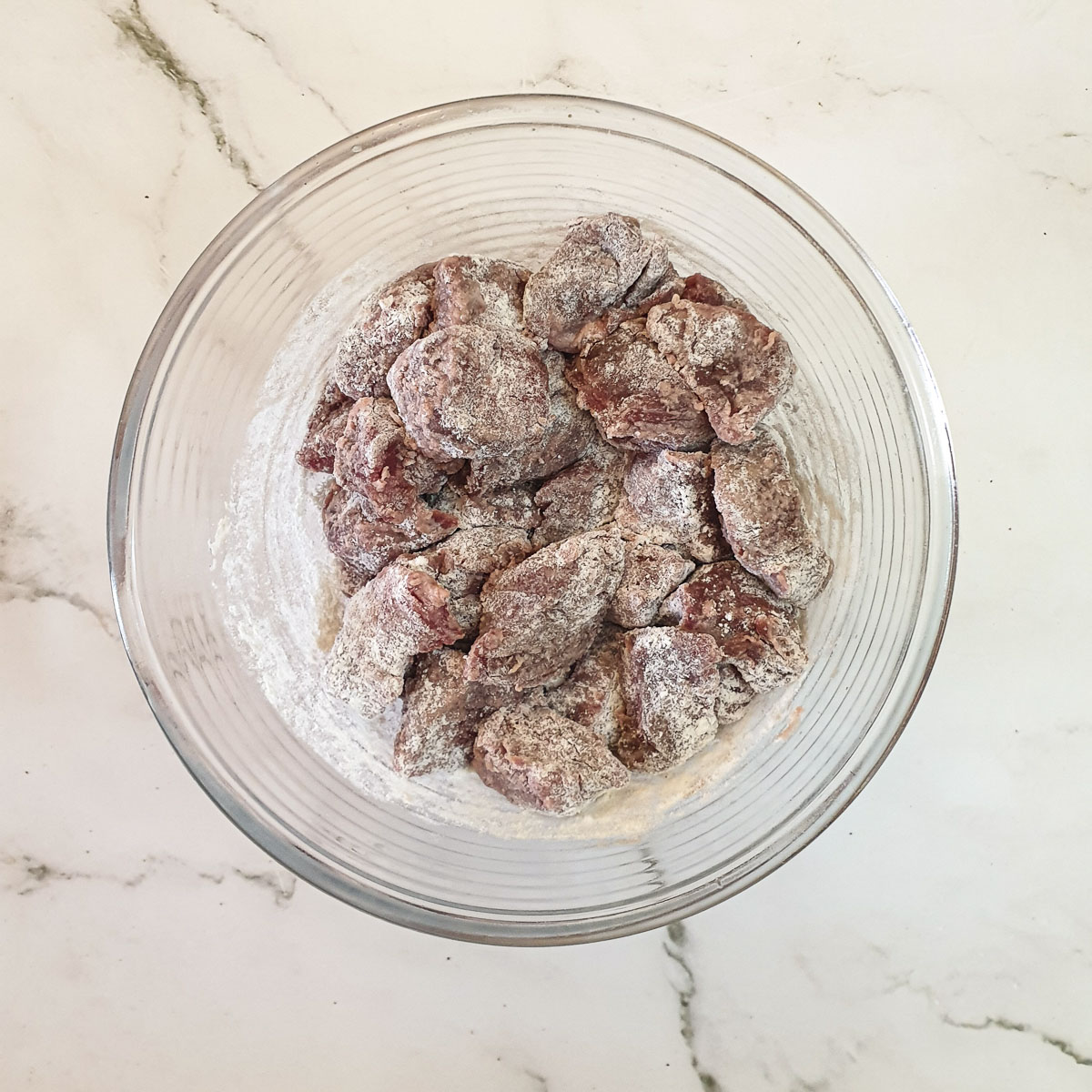 Beef cubes coated in flour in a glass mixing bowl.