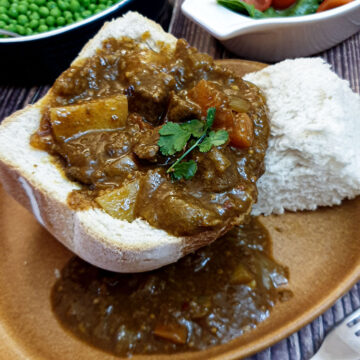 A hollowed-out loaf of bread on a plate, filled with beef curry.