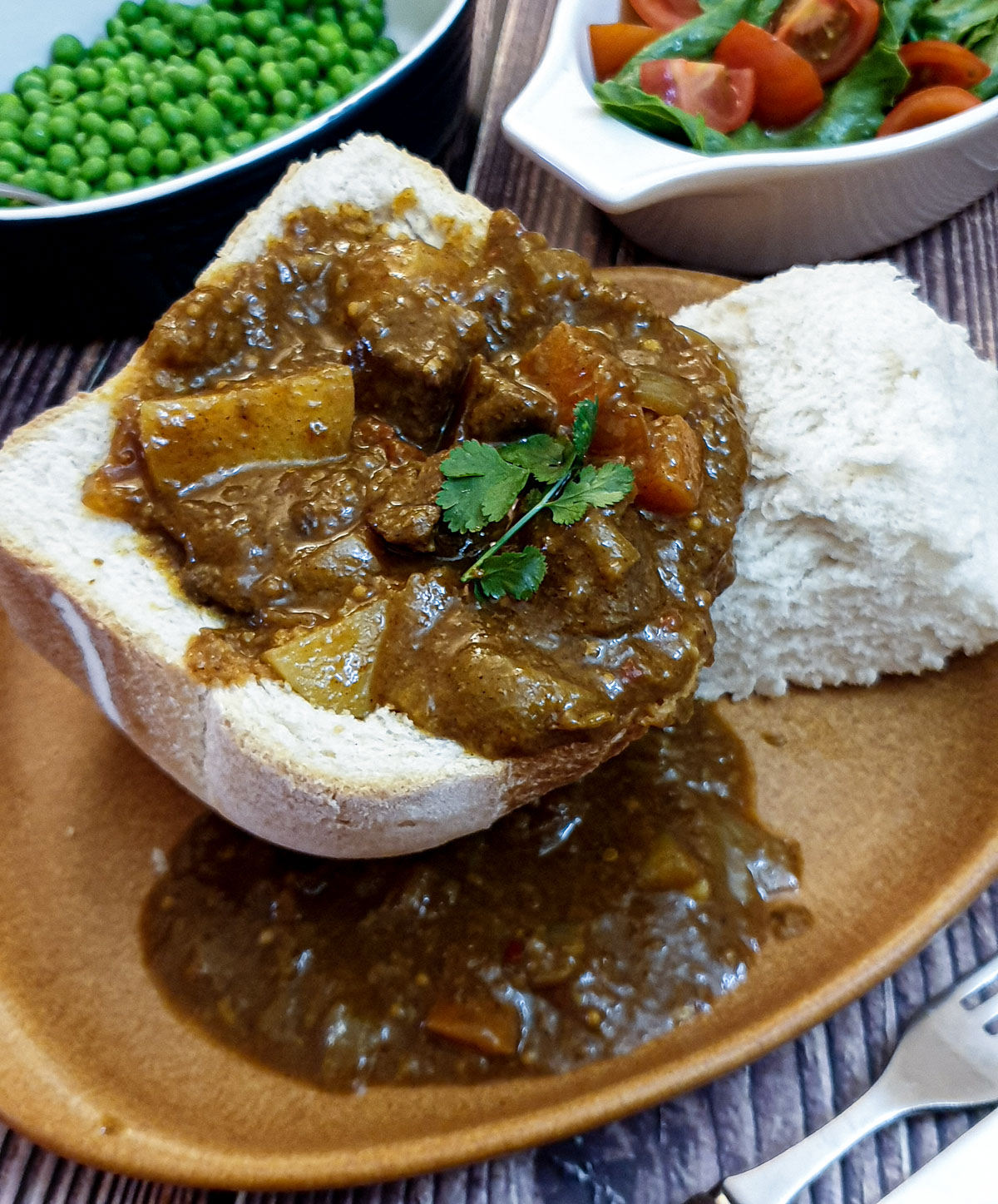 A hollowed-out loaf of bread on a plate, filled with beef curry.