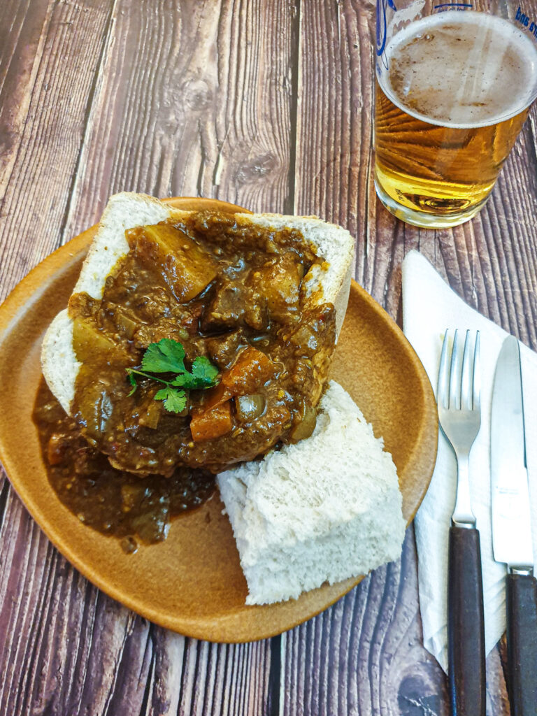 A hollowed-out loaf of bread on a plate, next to a glass of beer.